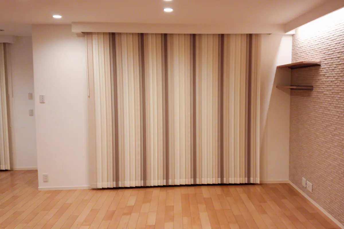 夜のリビング。縦型ブラインドを閉じ、コーニス照明(間接照明)で壁面を照らした落ち着いた空間。