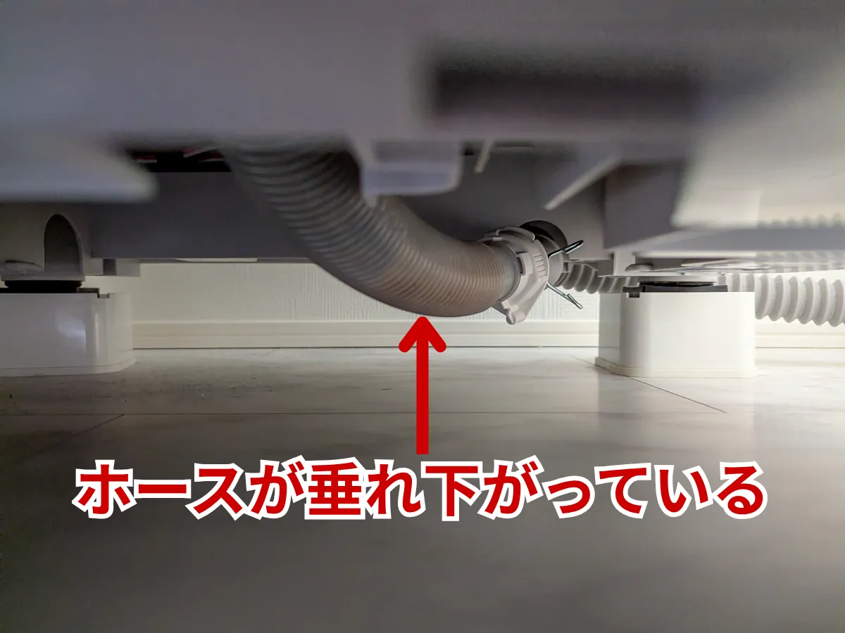 ドラム式洗濯機の排水ホースが床に垂れ下がり、逆勾配の「たるみ」ができている様子